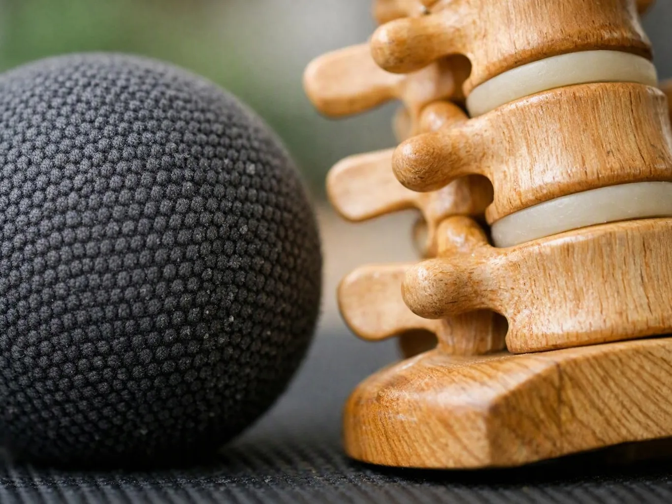 A black fabric-covered ball sits beside stacked wooden massage rollers on a textured surface
