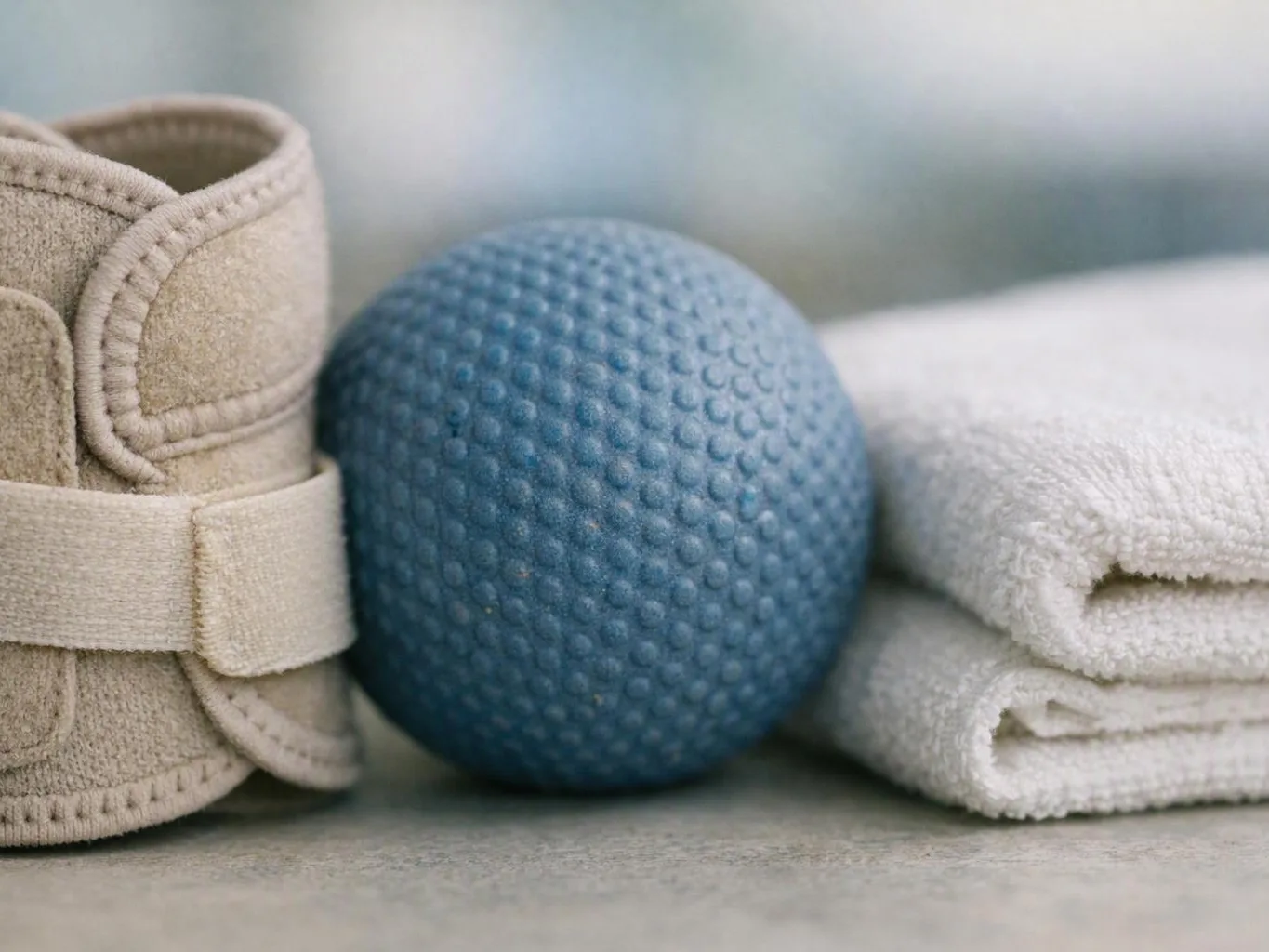 A blue textured massage ball sits between a rolled beige wrap and folded white towels