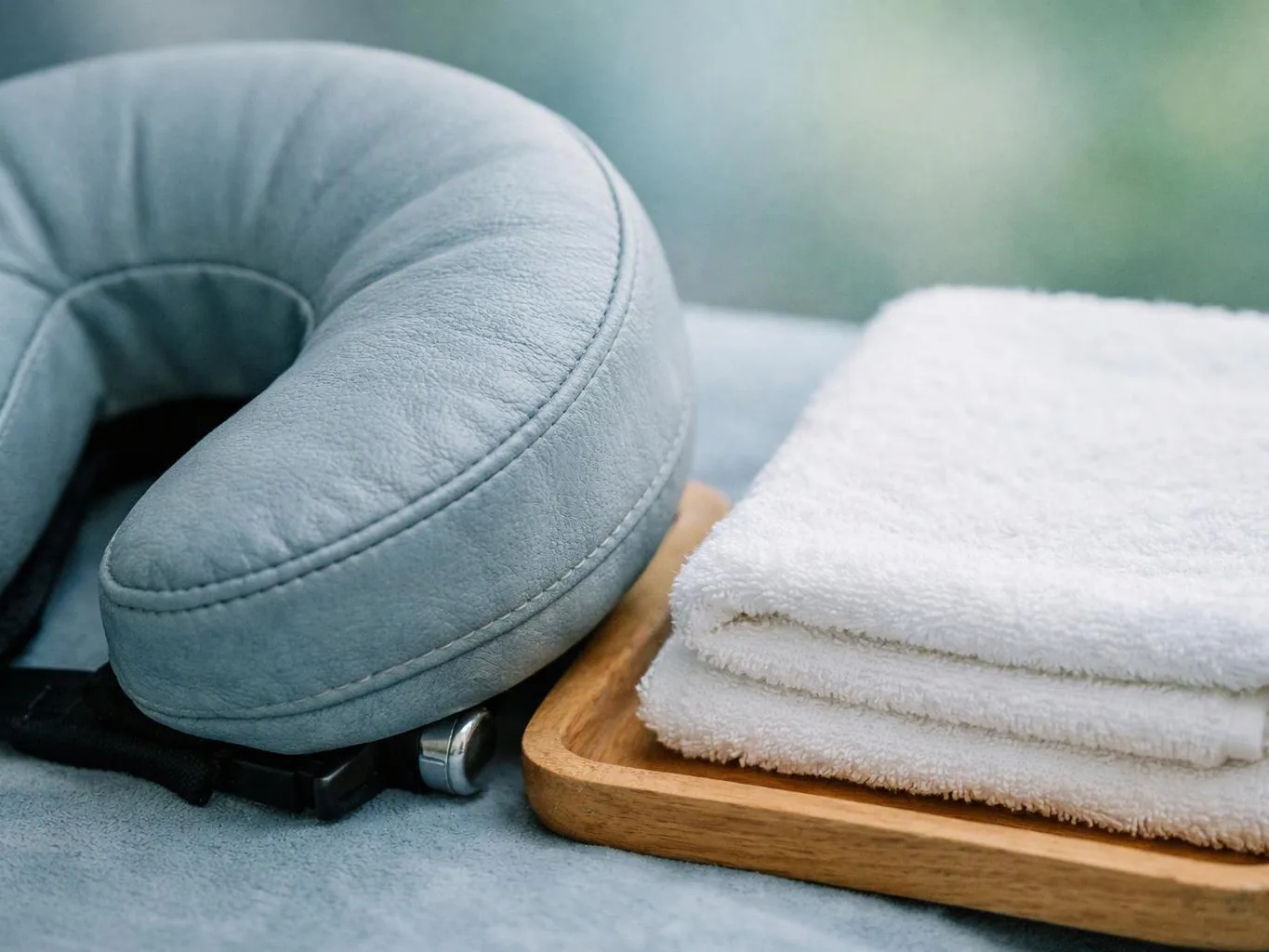 A folded blue neck pillow rests beside stacked white towels on a wooden tray