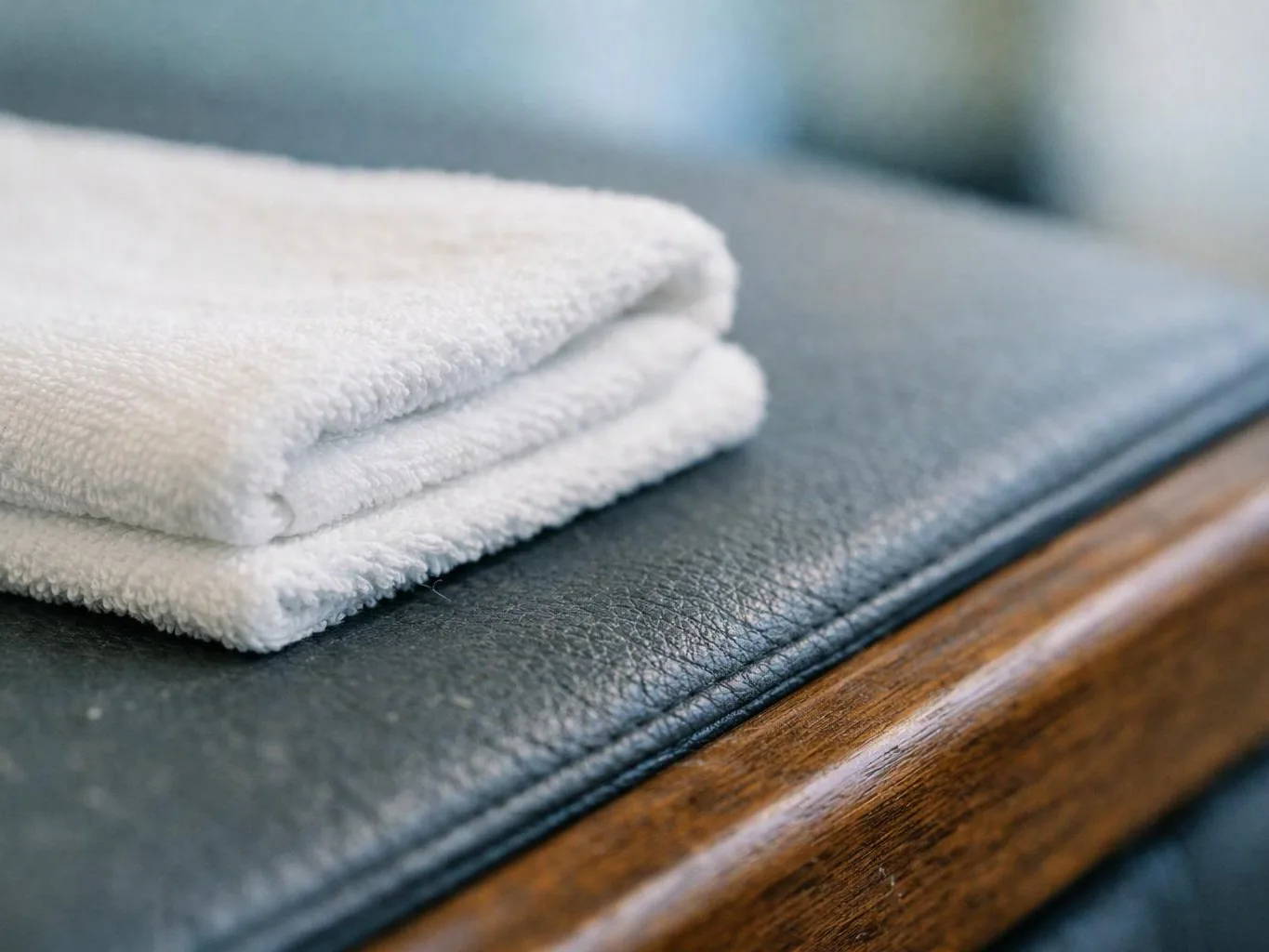 Folded white towels rest on a dark cushioned bench with a wooden edge